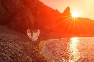 misterioso donna silhouette lungo capelli passeggiate su il spiaggia oceano acqua, mare ninfa vento ascolta per il onda. lanci su un' lungo bianca vestire, un' divine tramonto. artistico foto a partire dal il indietro senza un' viso