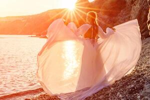 misterioso donna silhouette lungo capelli passeggiate su il spiaggia oceano acqua, mare ninfa vento ascolta per il onda. lanci su un' lungo bianca vestire, un' divine tramonto. artistico foto a partire dal il indietro senza un' viso