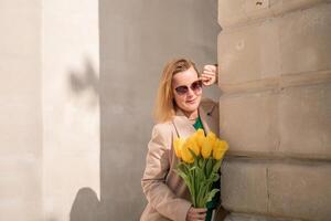 donna Tenere giallo tulipani, pendente contro pietra parete. Da donna vacanza concetto, dando fiori. foto