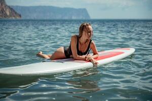 donna linfa mare. gli sport ragazza su un' tavola da surf nel il mare su un' soleggiato estate giorno. nel un' nero bagnarsi completo da uomo, lui bugie su un' linfa nel il mare. riposo su il mare. foto