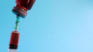 una siringa sporge da una bottiglia di liquido rosso. isolato su sfondo blu. medicina, iniezioni, vaccini e siringhe usa e getta, concetto di droga. bottiglia sterile. fiala di vetro medica per iniezione.