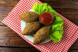 Kibbeh fritto con salsa di pomodoro su un piatto, su tavola in legno rustico foto