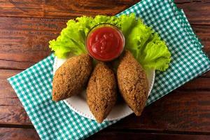 Kibbeh fritto con salsa di pomodoro su un piatto, su tavola in legno rustico foto