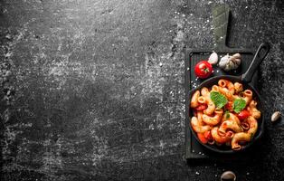 pasta nel padella su un' taglio tavola con aglio, pomodoro e menta le foglie. foto