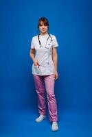 un' femmina medico, gesticolando, controlli il battito cardiaco nel il medico ufficio a il ospedale con un' stetoscopio isolato su un' blu sfondo foto