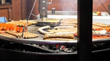 salsicce fritte. ristorante di strada. molte salsicce alla griglia su un grande barbecue rotondo in un festival del cibo di strada. barbecue grill al mercatino di Natale di bancarella di cibo. foto