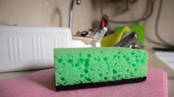 spugna verde e dispenser di sapone liquido per lavare i piatti su un lavandino sporco completamente con piatti e utensili da cucina. lavare i piatti in cucina a mano con detersivo e spugna. foto