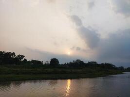 il sole è ambientazione al di sopra di un' fiume nel il distanza foto