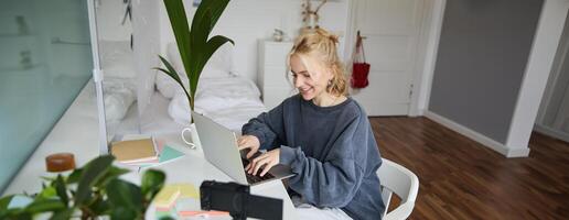 ritratto di donna seduta a scrivania con computer portatile, registrazione di se stessa su computer portatile, fabbricazione stile di vita per sociale media account foto