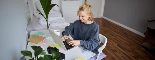 ritratto di giovane donna distanza apprendimento, Lavorando a partire dal casa con computer portatile, fabbricazione Appunti, alunno studiando su a distanza, fare in linea corso foto