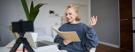 Immagine di giovane lungo donna, alunno studiando in linea a casa, si siede nel sua camera, legge Appunti, chat attraverso il computer portatile. frequenta corso, lavori su a distanza foto