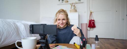 Immagine di giovane donna, vlogger record su digitale telecamera, Spettacoli bellezza prodotti, consigliare trucco per pubblico su sociale media, si siede su davanti nel un' camera foto