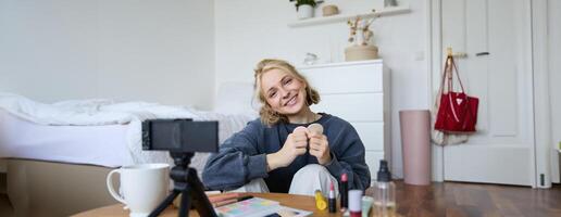 ritratto di sorridente giovane donna, seduta nel davanti di digitale telecamera nel accogliente impostato su, registrazione per stile di vita video blog, chat di trucco e bellezza prodotti foto