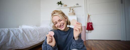 ritratto di felice, bellissimo biondo donna, mostrando trucco prodotti su telecamera, registrazione video blog, sociale media soddisfare per seguaci, in linea vivere ruscello di bellezza elementi foto