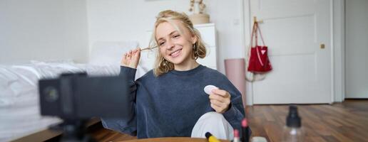 ritratto di sorridente giovane donna si applica trucco, Spettacoli bellezza lezione su , record video blog su digitale telecamera nel sua camera, raccomanda cosmetico prodotti foto