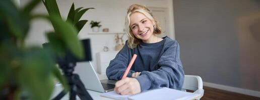 ritratto di giovane donna, stile di vita blogger, registrazione di se stessa, fabbricazione Appunti, scrittura nel rivista, seduta nel davanti di il computer portatile nel un' camera e studiando foto