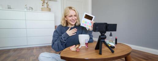 ritratto di bellissimo sorridente donna, registrazione nel sua camera, ha telecamera su caffè tavolo, rivedere trucco, fare stile di vita video blog per sociale media account, record un' lezione foto