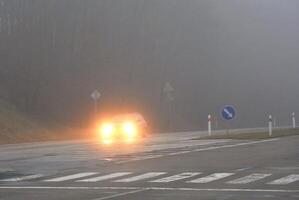 macchine nel il nebbia. cattivo inverno tempo metereologico e pericoloso automobile traffico su il strada. leggero veicoli nel nebbia. foto