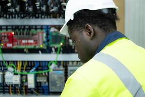 ritratto di un' tecnico Lavorando con un' digitale multimetro per test il elettrico sistema di un' enorme circuito tavola a un industriale pianta utilizzando un automatizzato mano robot. foto