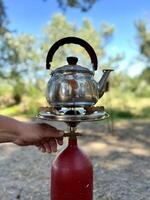 un' uomo prepara tè su un' portatile gas stufa all'aperto. preparazione prima colazione per un' picnic durante un' escursione. viaggio campeggio stile di vita concetto. foto