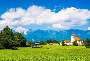 bellissimo villaggio alpino in slovenia. montagne e cielo nuvoloso. prato verde e la vecchia chiesa foto