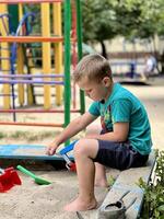 un' poco ragazzo giocando nel il sandbox a il terreno di gioco all'aperto. verticale foto