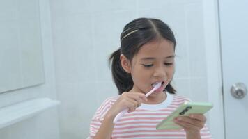 un' giovane ragazza è spazzolatura sua denti mentre guardare a sua Telefono foto