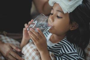 un' giovane ragazza è potabile acqua mentre indossare un' bendare su sua fronte foto