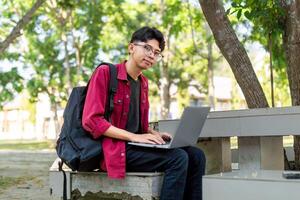 ritratto di asiatico Università alunno utilizzando il computer portatile guardare per telecamera. un' uomo Lavorando con un' il computer portatile computer a città universitaria foto