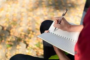 asiatico Università alunno studiando su il computer portatile a città universitaria all'aperto parco. uomo scrittura su un' Nota libro e Lavorando su il computer portatile. educativo concetto foto