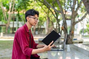 asiatico Università alunno lettura un' libro a il città universitaria parco. foto