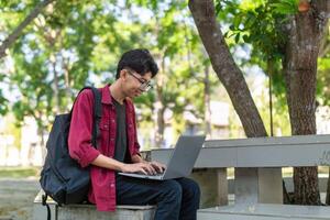 ritratto di asiatico Università alunno utilizzando il computer portatile guardare per telecamera. un' uomo Lavorando con un' il computer portatile computer a città universitaria foto