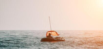 pescatore mare barca. turista manovra un gonfiabile barca mentre pesca nel un' vita giacca, con il bellissimo tramonto mare nel il sfondo. un' rilassante pesca viaggio. foto