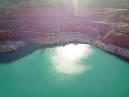 aereo superiore Visualizza su a cielo aperto estrazione cava con allagato parte inferiore, turchese superficie di il lago. cava stagno coperto di vegetazione con verde impianti e chiaro turchese acqua foto