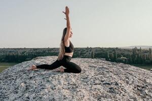 fitness donna. bene guardare mezzo anziano donna con lungo capelli, fitness istruttore nel ghette e cime fare allungamento e pilates su il roccia vicino foresta. femmina fitness yoga routine concetto. foto