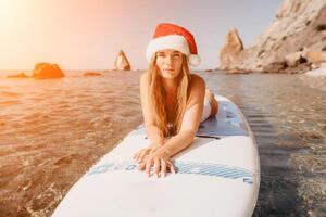 donna mare sup. vicino su ritratto di contento giovane caucasico donna con lungo capelli nel Santa cappello guardare a telecamera e sorridente. carino donna ritratto nel un' bianca bikini in posa su cenare tavola nel il mare foto