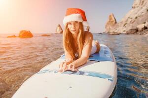 donna mare sup. vicino su ritratto di contento giovane caucasico donna con lungo capelli nel Santa cappello guardare a telecamera e sorridente. carino donna ritratto nel un' bianca bikini in posa su cenare tavola nel il mare foto