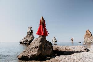 donna viaggio mare. giovane contento donna nel un' lungo rosso vestito in posa su un' spiaggia vicino il mare su sfondo di vulcanico rocce, piace nel Islanda, condivisione viaggio avventura viaggio foto