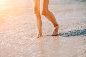 un' donna passeggiate lungo il spiaggia, gambe avvicinamento. a piedi nudi donna sta foto