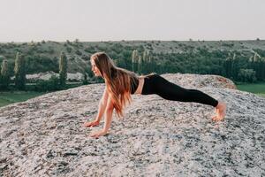 fitness donna. bene guardare mezzo anziano donna con lungo capelli, fitness istruttore nel ghette e cime fare allungamento e pilates su il roccia vicino foresta. femmina fitness yoga routine concetto. foto