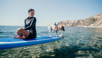 mare donna sup. silhouette di contento positivo giovane donna con sua cane, fare surf su cenare tavola attraverso calma acqua superficie. idilliaco tramonto. attivo stile di vita a mare o fiume. estate vacanza con animali domestici. foto