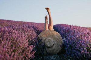 donna lavanda campo. contento spensierato donna gambe bastone su di il lavanda cespugli, caldo tramonto luce. cespugli di lavanda viola nel fiore, aromatico fiori a lavanda campi. foto