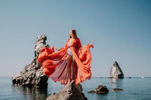 donna viaggio mare. giovane contento donna nel un' lungo rosso vestito in posa su un' spiaggia vicino il mare su sfondo di vulcanico rocce, piace nel Islanda, condivisione viaggio avventura viaggio foto