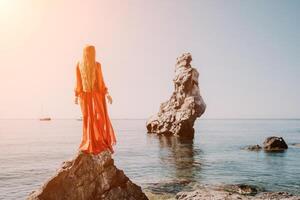 donna viaggio mare. giovane contento donna nel un' lungo rosso vestito in posa su un' spiaggia vicino il mare su sfondo di vulcanico rocce, piace nel Islanda, condivisione viaggio avventura viaggio foto