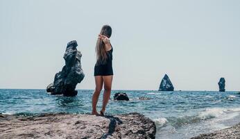 donna estate viaggio mare. contento turista nel cappello godere assunzione immagine all'aperto per ricordi. donna viaggiatore in posa su il spiaggia a mare circondato di vulcanico montagne, condivisione viaggio avventura viaggio foto