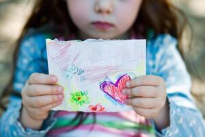 poco ragazza dando sua mano scrittura saluto carta per sua mamma. foto