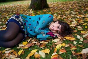 un' ragazza nel un' vestito con palloncini bugie su il terra coperto con autunno le foglie foto
