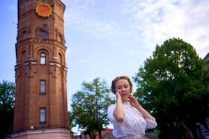 elegante giovane donna nel un' bianca Vintage ▾ vestito su il piazza vicino il storico acqua Torre nel vinnytsia foto