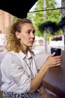 un' bellissimo mezzo età donna nel anni '70, anni 80 stile Abiti bevande caffè seduta a il bar nel un' moderno bar foto