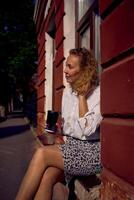 mezzo età donna nel anni '70, anni 80 stile Abiti con un' caffè macchia su sua camicia bevande caffè seduta su il davanzale foto